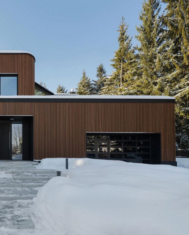 Гаражный фрагмент дома с брусковыми панелями ДПК, снег у основания и чистые чёткие линии фасада, подчёркивающие современную архитектуру.