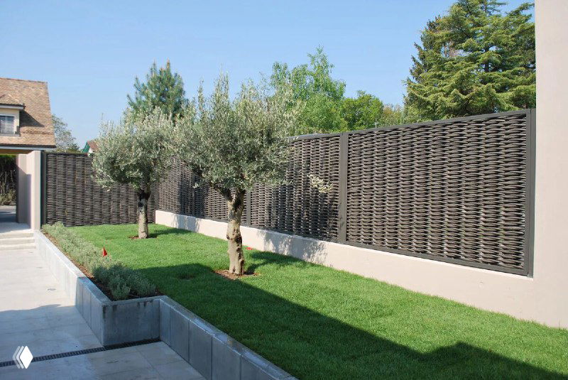 Современное декоративное полимерное ограждение тёмного цвета рядом с ухоженным газоном; подчёркивается аккуратный современный вид и текстура материала.