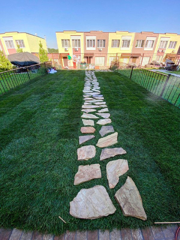 Готовый рулонный газон у таунхауса с каменной тропинкой посередине: плотная зелёная трава, аккуратно уложенные рулоны.