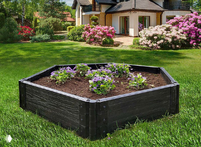 Поднятая декоративная грядка с цветами на ухоженном зелёном газоне перед загородным домом — идея компактной декоративной клумбы на участке.