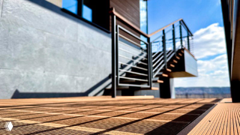Крупный план террасного покрытия и металлической лестницы, текстура доски ДПК, игра тени на поверхности при солнечном свете.