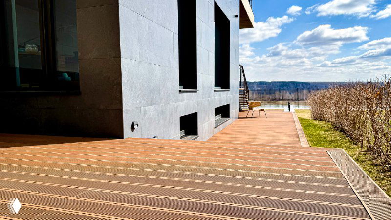 Широкий план террасного настила вдоль фасада дома, вид на ровную поверхность и аккуратную укладку досок без дефектов.