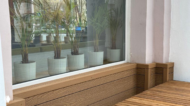 Уголок у витрины Port Coffee: низкий бортик и настил из Polivan, на подоконнике ряд горшков с растениями, создающими уютную атмосферу.