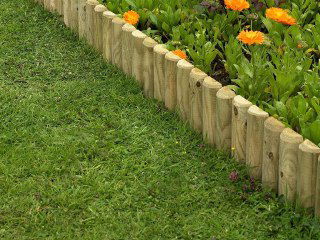 Низкий декоративный деревянный заборчик вдоль газона и клумбы с цветами, подчёркивающий аккуратный край участка.