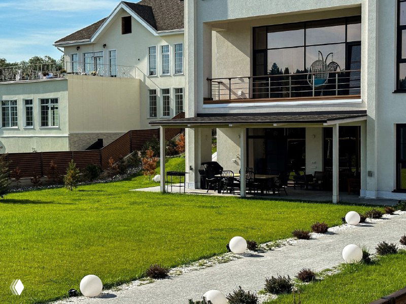 Современный рулонный газон с полосой гравия и декоративными светильниками у фасада дома, аккуратный минималистичный дизайн.