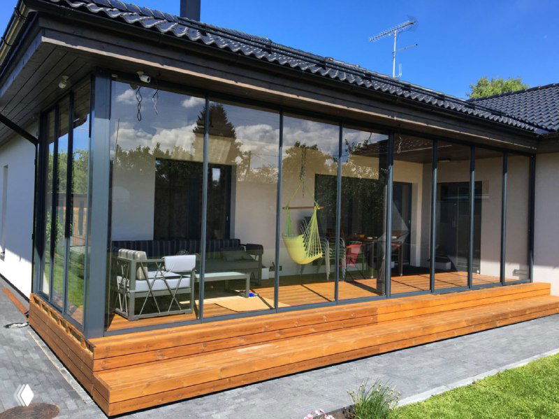 Терраса с панорамным остеклением и раздвижными створками: стеклянные стены, вид на интерьер и подвесное кресло внутри.