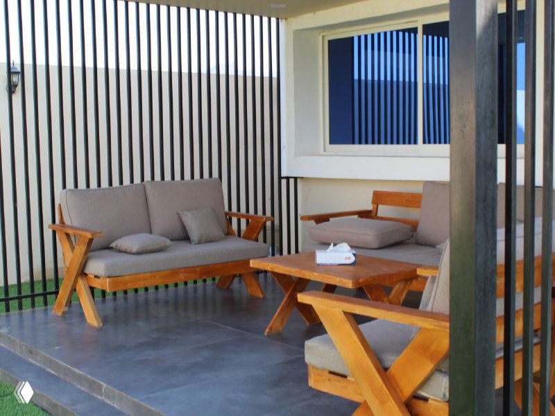 Уютная лаунж-зона на террасе с декоративной перегородкой из вертикальных реек и деревянной садовой мебелью.