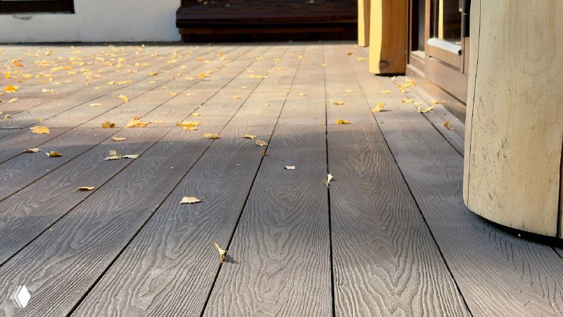 Низкий ракурс настила: текстура коричневой террасной доски Polivan SINGARAJA с осенними листьями и опорами мебели