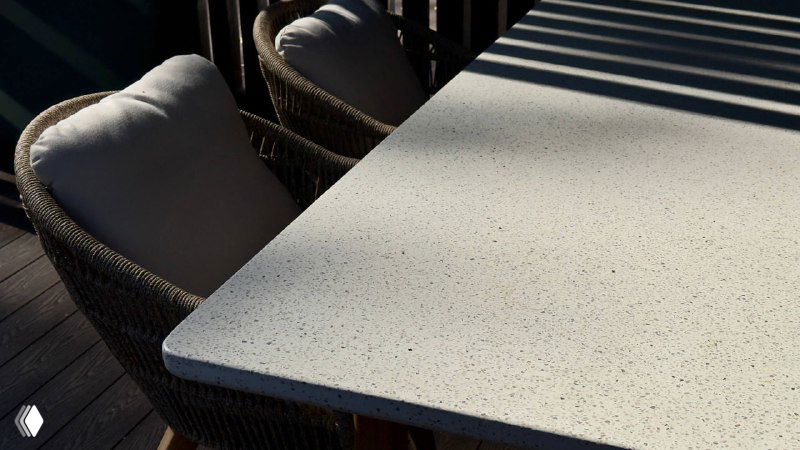 Фрагмент обеденного стола и кресел TALARA: столешница светлая, кресла с подушками, тени от перголы падают на мебель