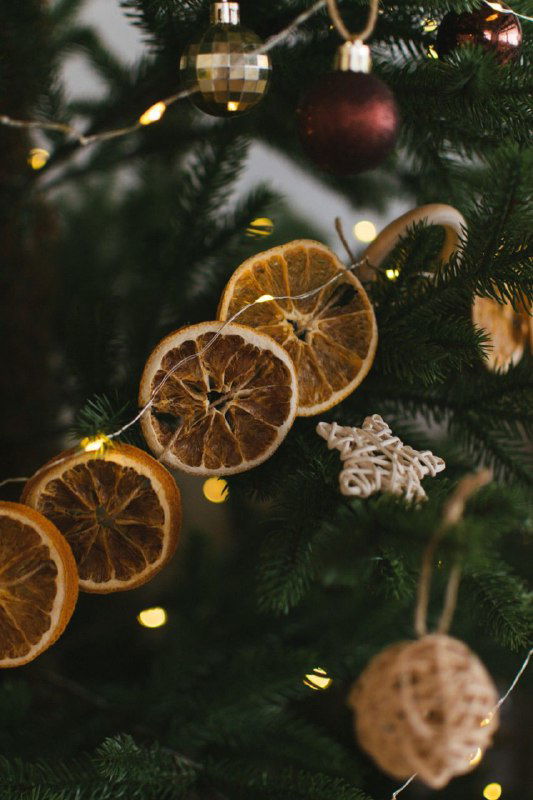 Гирлянда из сушёных цитрусов и шишек на еловых ветках: сухие дольки апельсина, шишки и мягкое тёплое праздничное освещение на фоне хвои.