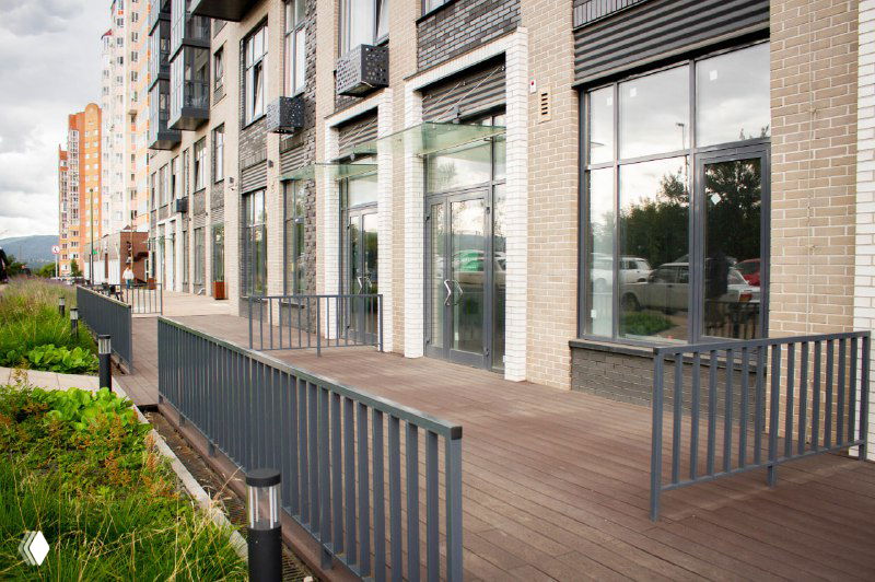 Крупный план настила вдоль входной группы жилого дома: ровная укладка коричневых досок Polivan SINGARAJA и металлическое ограждение