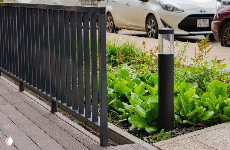 Зона озеленения с приподнятой клумбой рядом с настилом и ограждением; видна структура доски и окружающий благоустроенный тротуар