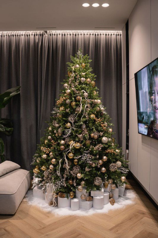 Ёлка в уютной гостиной, украшенная пастельными шарами и серебристыми гирляндами; под ёлкой аккуратно уложены подарки в светлой упаковке.
