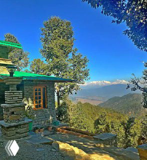 Каменный домик в предгорьях с видом на долину и отдалённые снежные вершины под ясным синим небом, мотив для переезда.