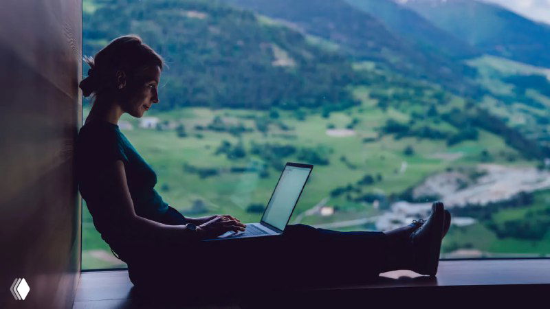 Силуэт человека с ноутбуком на подоконнике — удалённая работа на фоне зелёной горной долины и реки; спокойная атмосфера для примера ВНЖ/удаленки.