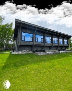 Длинное тёмное здание апартаментов или коттеджей на фоне газона и неба, аккуратный ландшафт вокруг комплекса.