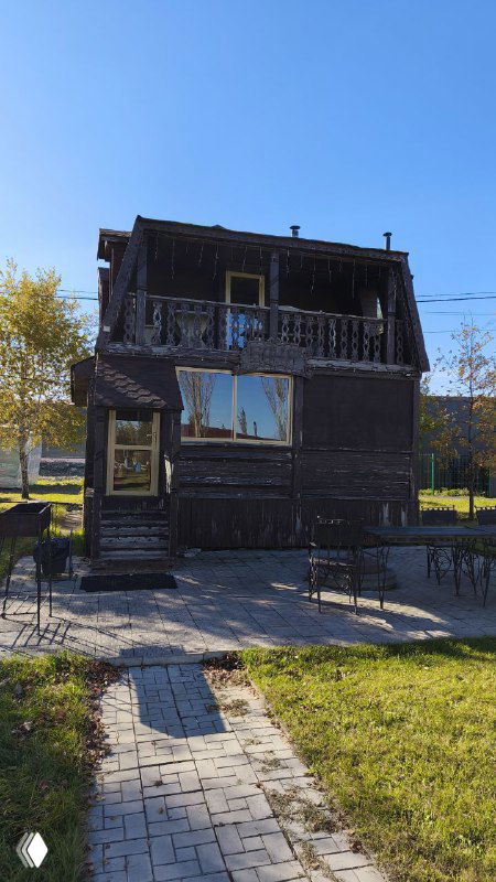 Двухэтажное деревянное строение и прилегающая дорожка на территории базы отдыха, тёплая атмосфера загородного комплекса.