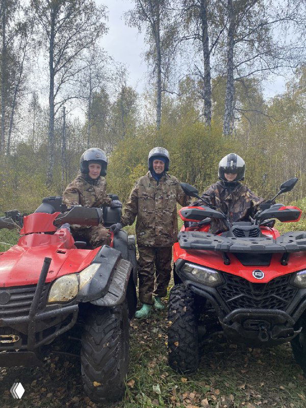 Трое участников в камуфляже стоят между двумя красными квадроциклами в лесной полосе, видны берёзовые деревья и подготовка к маршруту.