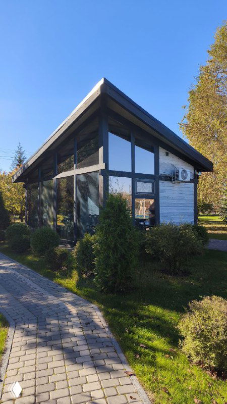 Современное здание с большими окнами среди зелёных насаждений и садовой дорожкой, часть инфраструктуры базы отдыха.