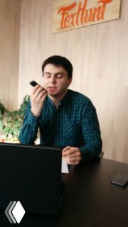 Мужчина в клетчатой рубашке делает холодный звонок за рабочим столом с ноутбуком, держит смартфон у рта в офисе.