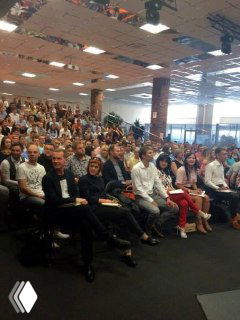 Фотография большой аудитории конференции: заполненный зал участников, люди сидят в рядах, видна сцена и общий масштаб мероприятия.