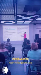 Скрин с видео доклада: спикер на сцене показывает слайд, перед ним аудитория, на экране и внизу подпись с именем докладчика и темой.