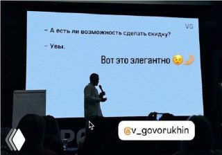 Фото презентации: силуэт докладчика на фоне слайда с диалогом про просьбу скидки и подписью «Вот это элегантно», аудитория в полумраке.