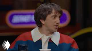 Кадр из видео: мужчина в ярком свитере сидит в студии во время беседы, крупный план лица, размытый фон.