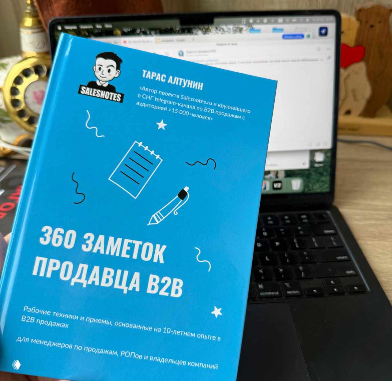 Фотография подписанной печатной книги «360 заметок продавца В2В» на фоне ноутбука; видно голубую обложку, логотип Salesnotes и рабочий стол.