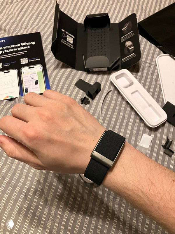 Whoop 5.0 на запястье автора во время распаковки: браслет на руке, рядом видны комплектующие и открытая упаковка.