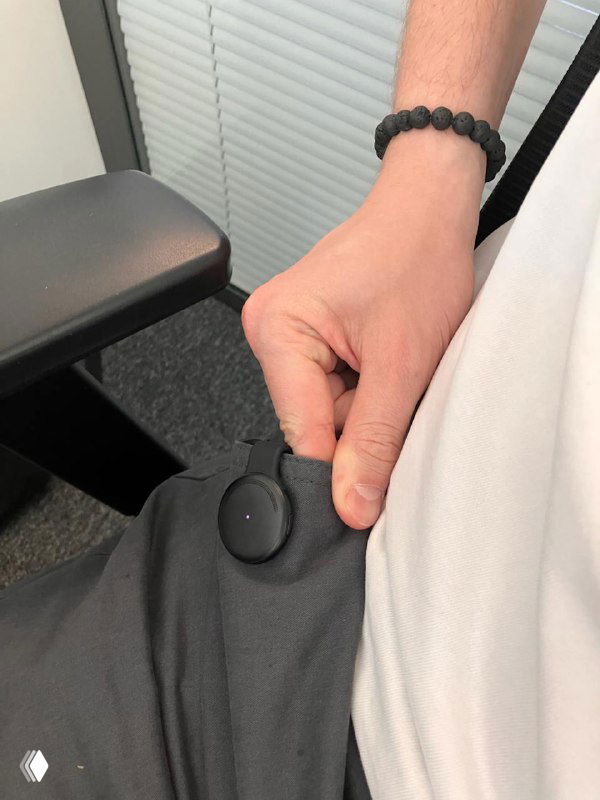 Крупный план: человек крепит Limitless Pendant на одежду у пояса, показан способ фиксации магнитами и резинкой, съёмка в офисной обстановке.