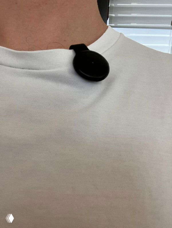 Pendant на шее: крупный план аксессуара на белой футболке человека, видна верёвочная подвеска и компактный круглый корпус устройства.