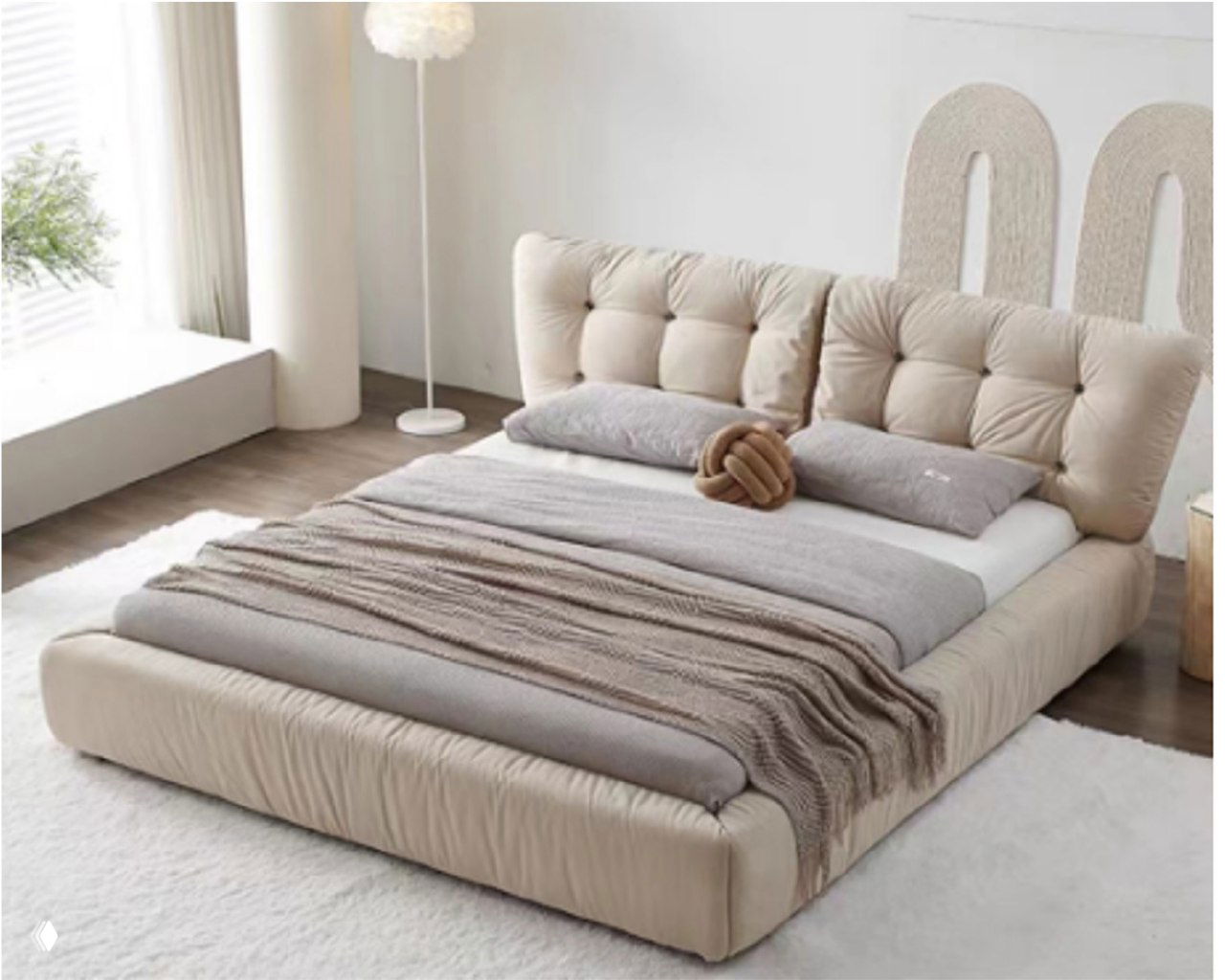 Мягкая бежевая кровать в светлой спальне с высоким капитонированным изголовьем, мягкими подушками и пледом.