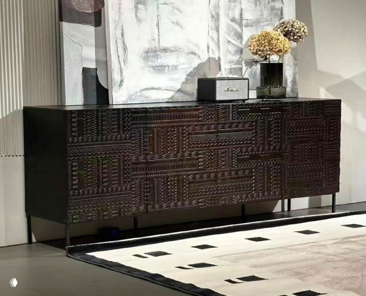 Тёмный комод из массива ясеня с резным геометрическим узором в современном интерьере — ковер на полу, ваза и картина на поверхности