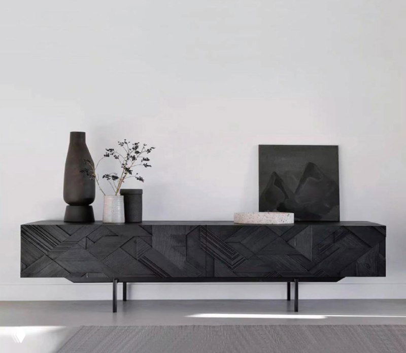 Тёмная тумба под ТВ из массива ясеня в минималистском интерьере: низкий комод на ножках с резным фасадом, вазы и панно.