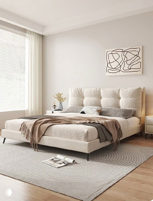 Бежевая мягкая кровать в светлой минималистичной спальне: изголовье с мягкими секциями, ковёр на полу, естественный свет из большого окна.