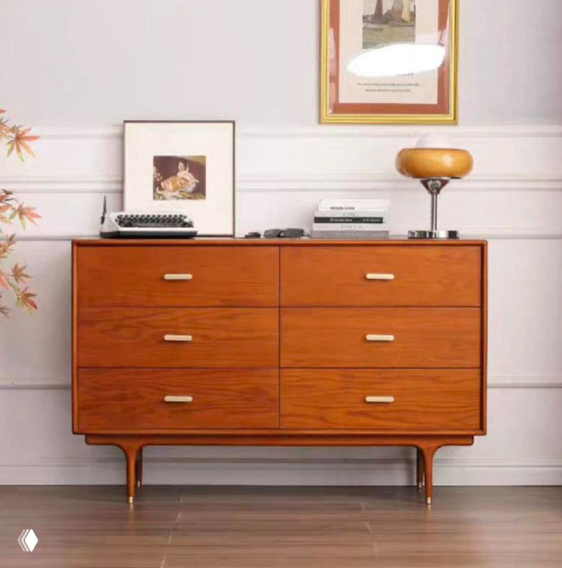Комод из ясеня в жилом интерьере: шесть выдвижных ящиков, тёплое древесное покрытие, латунные ручки и настольная лампа сверху на фоне светлой стены.