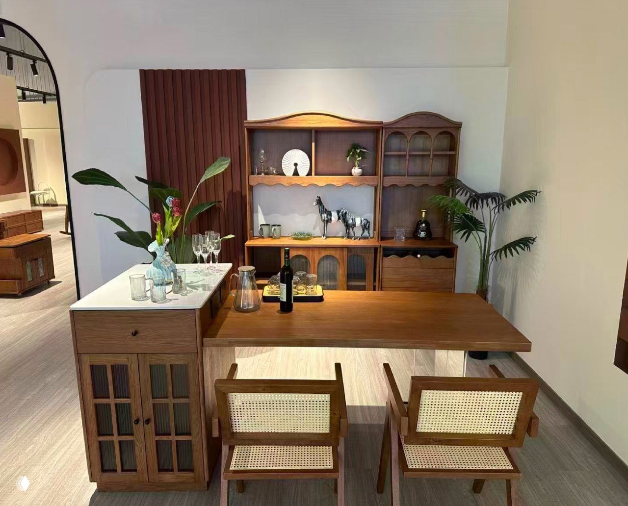 Выставочный образец стола из массива ясеня в шоуруме: деревянная столешница, две плетёные стулья, сервант и декоративные детали на фоне, нейтральное освещение.