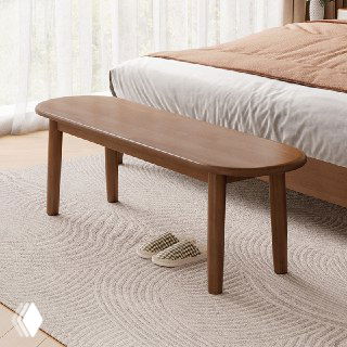 Деревянная лавочка из дуба в светлой спальне на ковре рядом с кроватью и тапочками; демонстрация текстуры, формы и тёплого цвета изделия.