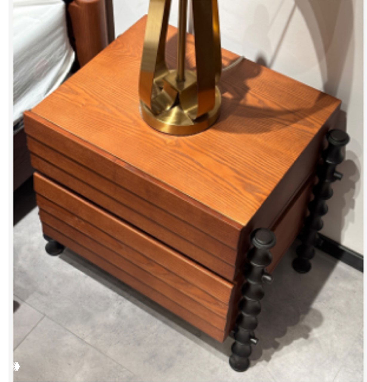 Фото прикроватной тумбочки из массива ясеня с текстурой древесины, выдвижными фасадами и чёрными декоративными ножками.