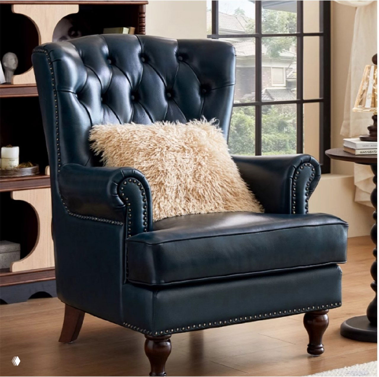 Темно-синее кожаное кресло в классическом стиле с капитоне на спинке, пушистой декоративной подушкой и деревянными ножками в уютной гостиной у окна.