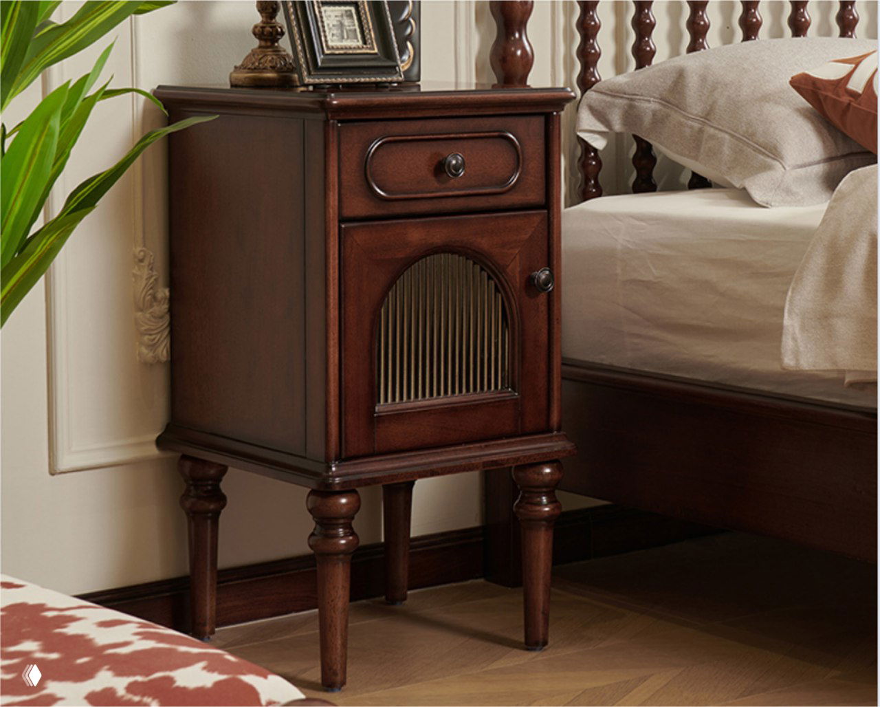 Прикроватная тумбочка из массива дуба тёмного тона рядом с кроватью, крупный план с акцентом на ножки и текстуру дерева.