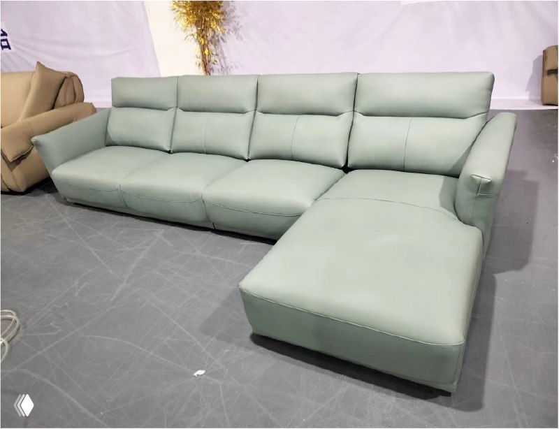 Фотография углового светло-зелёного кожаного дивана в шоуруме: вид спереди, chaise longue справа, видно обивку, подушки и общую форму.