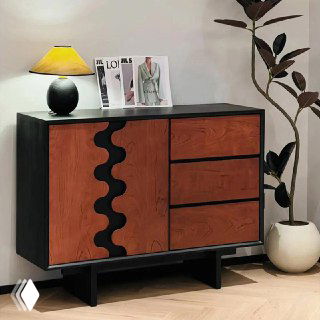 Комод из дуба в интерьере: тёмная рамка, фасады с деревянным рисунком и декоративным волнообразным элементом, лампа и растение рядом.