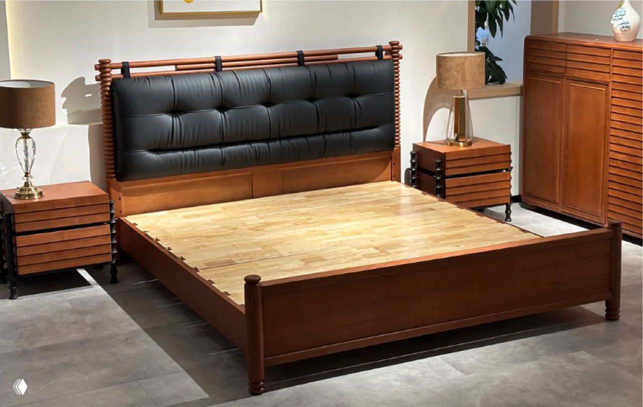 Кровать из массива ясеня в шоуруме, деревянная рама и основание, высокое чёрное мягкое изголовье, тумбочки и шкаф на фоне.