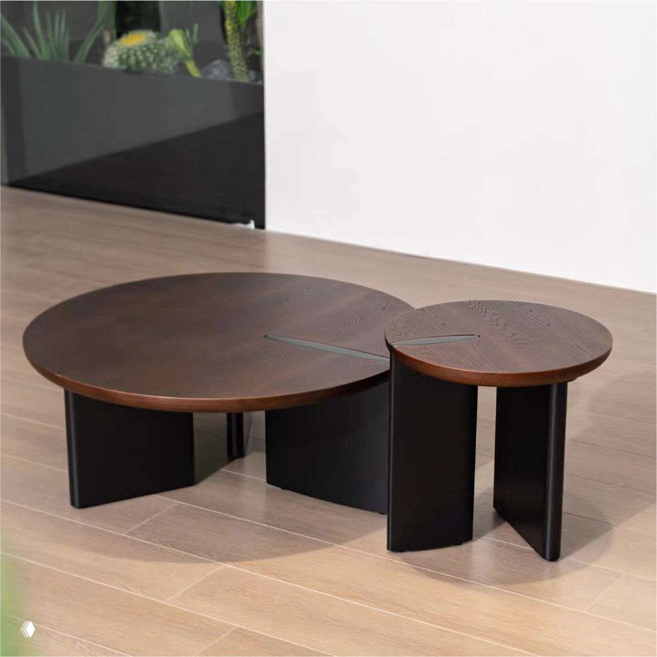 Круглый журнальный столик из массива дуба тёмного оттенка на низких чёрных опорах, фото товара в светлом интерьере с деревянным полом и растениями