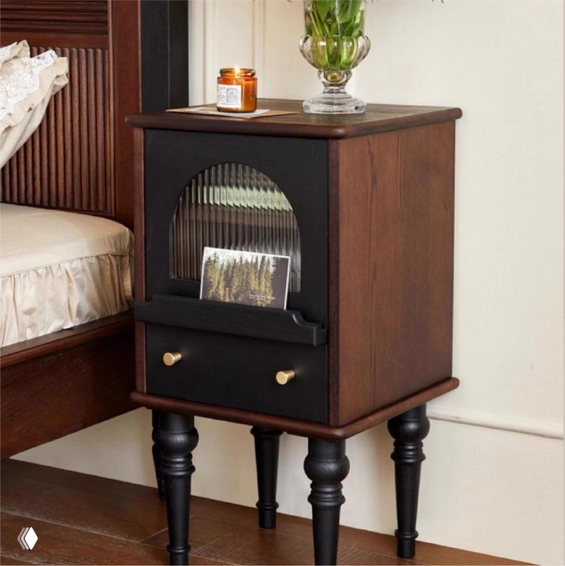 Фото прикроватной тумбочки из массива дуба в интерьере спальни: тёмно-коричневый корпус, фигурные чёрные ножки и выдвижной ящик.