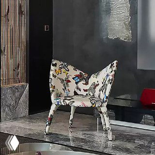 Фотография кресла с цветочной тканевой обивкой и декоративным узором на ножках, размещённого в современном интерьере для демонстрации дизайна и текстуры
