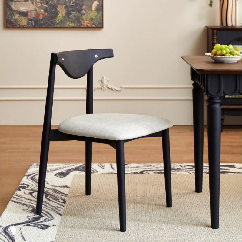 Деревянный обеденный стул из массива дуба с светлой мягкой обивкой, на ковре рядом с обеденным столом в интерьере.