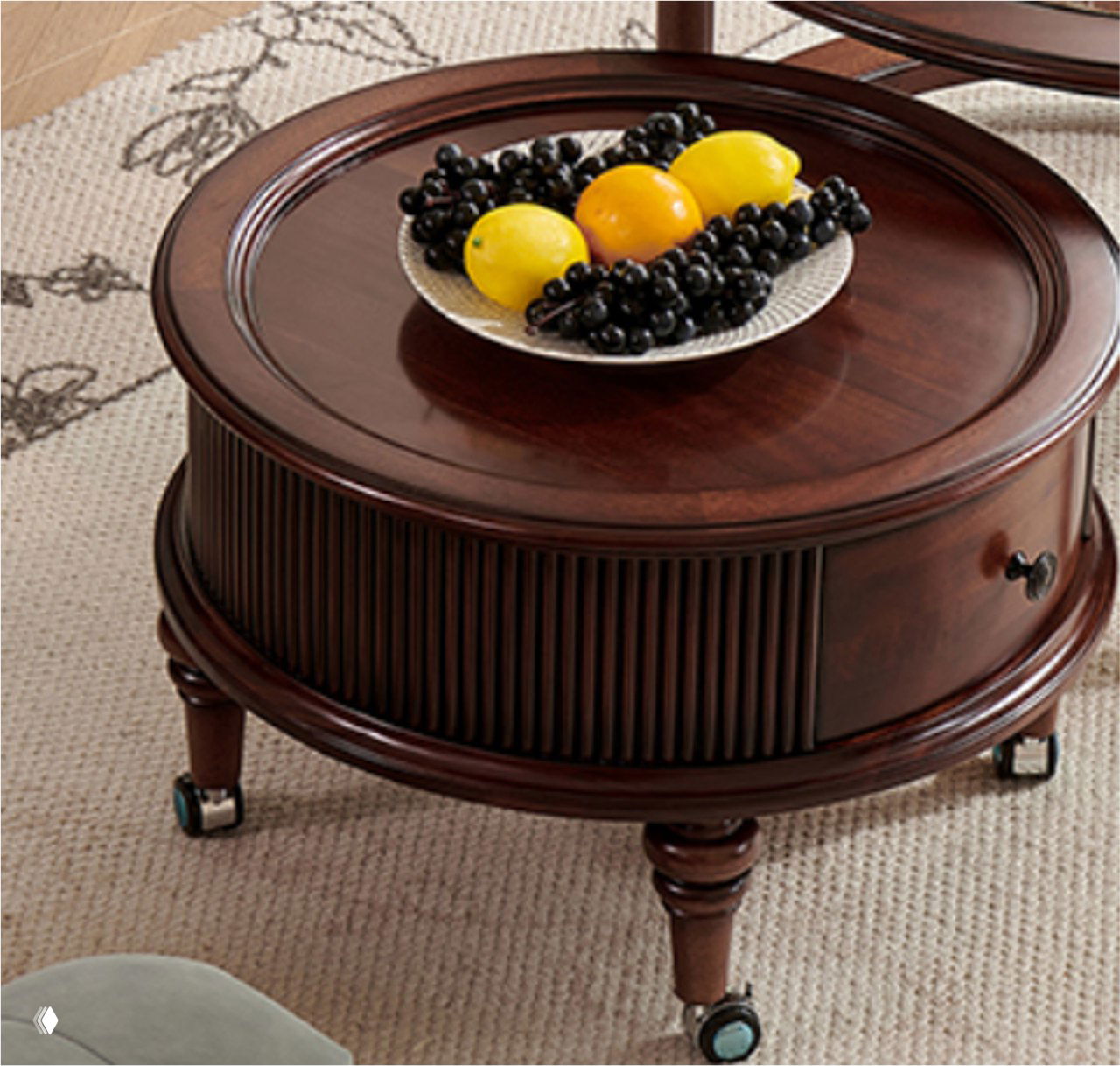 Крупный план круглого журнального столика из массива тёмного дуба на колесиках; сверху тарелка с фруктами, ковёр на фоне.